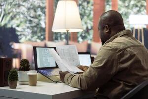 Businessman searching for commercial office spaces from his home workstation, doing a blueprints review and drafting building layouts to find the perfect startup property. Real estate. photo