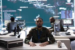 Military officer conducting a remote conference on secure network to share important information for field troops, helping with intelligence from satellite radar systems. Mission control center. photo