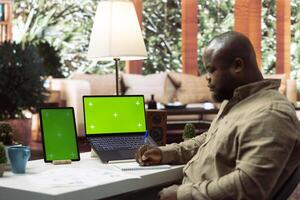 Focused expert takes notes and looks at isolated copy space screen, ensuring accounting balance for sales numbers. Entrepreneur increasing the business profit at his house. Infographics. photo