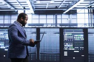 African american man in data center monitoring system performance, identifying bottlenecks and implementing optimizations to improve efficiency. Server hub professional troubleshooting bugs photo