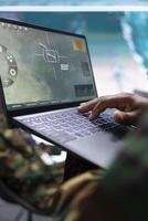 Military expert in a control center uses advanced technology on laptop, overseeing satellite imagery and surveillance systems to support strategic missions. Monitor potential national threats. photo