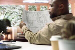 Businessman studying architectural blueprint plans at home office, using digital tools to review and plan office spaces for relocation. Business development strategy with property renting. photo