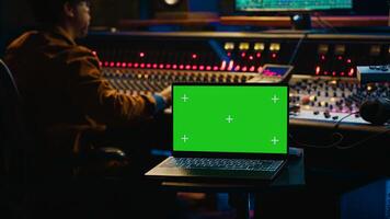 African american artist working with mockup on display in control room, mixing and mastering tracks with audio console and buttons or knobs. Music producer recording and editing sounds. Camera A. photo