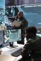 Army professional in command center talks on phone call and gives crucial information, overseeing satellite data in real time. Protect national security and support strategic military missions. photo