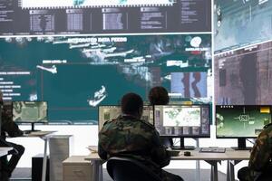 Army staff examining surveillance footage on big screen in operation room, gathering intelligence for a new defense mission. Diverse group of troopers working on reconnaissance activity. photo