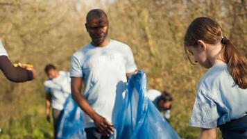 Diverse volunteers collecting garbage and junk from the forest area, fighting environmental pollution and conservation. Group of activists cleaning up the woods, recycling plastic waste. Camera A. photo