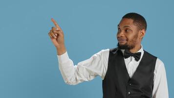 Doorkeeper bellhop pointing at something to left or right sides, indicating the direction for multiple amenities at the five star resort. Bellboy staff wearing a tuxedo uniform at his job. Camera A. photo