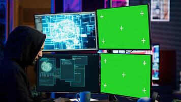 Hacker using AI and green screen computer monitors to produce malicious malware corrupt company data. Evil man working on mockup desktop PC using artificial intelligence, infecting systems, camera A photo