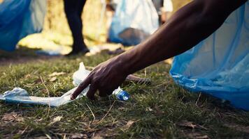 People supporting cleanup of the natural environment by grabbing recyclables and trash objects from the woods, collecting in a garbage bag. Using utensils to pick up rubbish. Close up. Camera B. photo