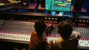 Musician and audio technician collaborating on mixing tracks to create a successful hit in professional studio. Team of experts listening to recordings and adding effects in post production. Camera B. photo