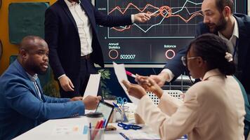 Project team colleagues examining sales infographics on presentation, reviewing annual reports to understand what needs to change in order to expand the business internationally. Camera A. photo