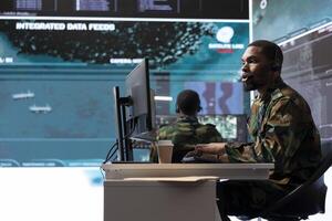 Military intelligence specialist using modern satellite systems and real time data to ensure national defense operations in a high tech control center base. Army professional working at computer. photo