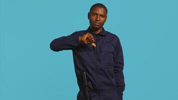 Portrait of security agent doing thumbs down sign gesturing, refusing entry while securing assigned post, studio background. Guardian doing negative hand gesture, handling security breaches, camera B photo