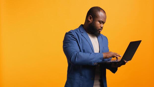 African american man using laptop to do business related tasks for company, isolated over studio background. Office clerk doing budgeting, forecasting, and financial analysis on notebook, camera B photo