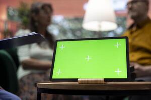 Caretaker offers professional advice to her elderly patients next to green screen on tablet, consulting senior couple during a home visit. Medical assistant provides support and medication. photo