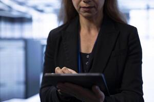 Programmer in data center implementing backup solutions to protect against data loss using tablet, ensuring efficient recovery processes. Server farm employee resolving technical issues photo