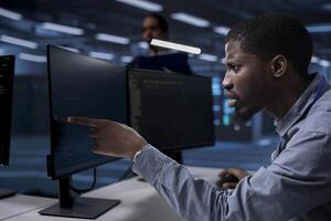 Server hub technician frowning, confused by errors on screen while shielding data from potential threats. Surprised african american man puzzled by malfunctions on data center hardware photo
