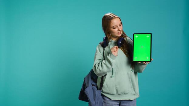 Portrait of woman presenting tablet with chroma key display, isolated over studio background. Young girl creating promotion with blank copy space mockup digital device, camera B photo