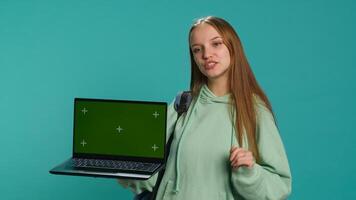 Happy girl presenting laptop with green screen display, isolated over studio backdrop. Radiant teenager creating promoting advertisement with mockup notebook device, camera A photo