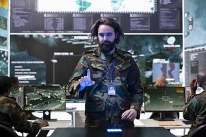 Young soldier collecting battlefield data and details for a new mission, employing a hologram projection in monitoring room. Recruit examines briefings on 3d holographic visualization. photo