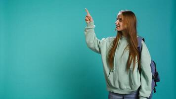 Radiant woman pointing finger towards empty space doing advertising, talking with audience. Smiling young girl doing presentation, showing copy text, studio backdrop, camera B photo