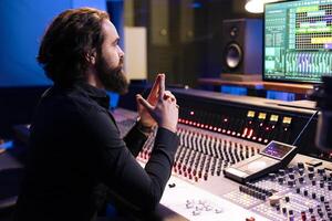 Tracking expert processing new songs with digital audio software and mixing console in studio, working in post production to create music. Sound engineer uses motorized faders and knobs. photo
