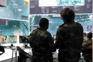 Diverse team of military personnel analyzing battlefield real time data on CCTV radar satellite system, transmitting information to soldiers in the field. Army superiors work on defense program. photo