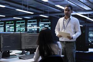 Data center inspector asks worker to show him emergency procedures paperwork, ensuring company is protected against system failure. Supervisor in server hub verifies industry regulations are respected photo