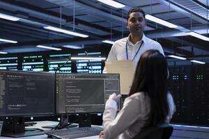 Team of engineers in data center looking for firewall misconfigurations affecting servers. Multiracial workers in server room check systems bottlenecks leading to sluggish data transfer rates photo