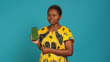 Young confident woman presenting a green screen on smartphone, working in studio on an advertisement. Smiling natural girl holds a phone with isolated chroma key display. Camera A. photo