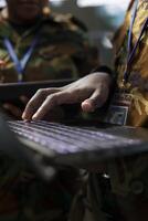 Army personnel operates on laptop to collect information from satellite footage, using world map projection to monitor activity. Gather intelligence for troops in the field. Close up. photo