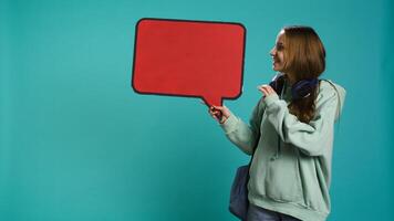 Smiling woman holding red speech bubble sign of empty copy space for message. Joyous teenager presenting thought bubble cardboard used as promotion concept, isolated over studio background, camera B photo