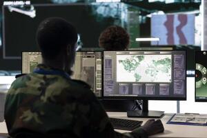 Army conscript serving his country by working in reconnaissance and espionage division, gathering crucial battlefield mission data. Trained trooper operates on computer and big screen in command post. photo