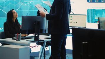 General director CEO sharing insight about a new development strategy with his employees, showing important data reports to analyze organizational activity status in a control room. Camera A. photo