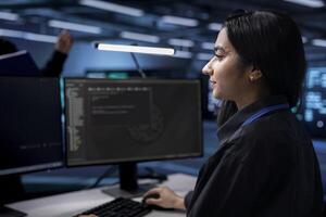 Indian technician in data center updating systems to keeps performance up and protect servers from exploitable software vulnerabilities. Woman looking for errors causing equipment to slow down photo