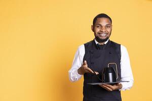 Skilled waiter bringing the teapot to the clients table to serve them tea before their meal order, service oriented industry. Employee with apron serves customers for satisfaction. photo