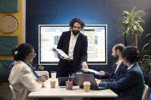 During an organizational reporting conference, group manager distributes papers with current statistics on performance. Team leader debates productivity at work and optimization. photo