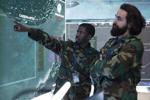 Team of recruits examining new surveillance footage on a big screen, gathering intelligence from satellite radar system in military monitoring room. GPS tracking on a world map, navy division. photo