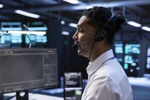 IT staff member in data center supporting engineering team doing equipment maintenance, talking in headset microphone. Worker in server room coordinating technicians using mic photo