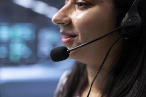 Expert in data center call center talking in headset microphone, providing logistics support. Close up of IT staff member in server farm communicating with engineers using mic photo