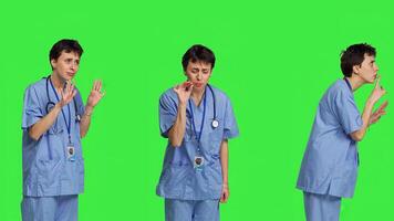 Medical assistant asking to keep quiet and be silent against greenscreen, showing hush mute symbol to keep privacy and silence. Young nurse showing secrecy taboo sign. Camera B. photo