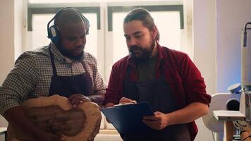 Woodworker looking over blueprints on laptop, brainstorming with colleague next steps in wood processing. Manufacturer and BIPOC apprentice reading furniture assembly schematics in studio, camera A photo