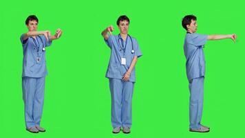 Displeased medical assistant shows thumbs down in studio, presenting her disapproval and disagreement with dislike symbol against greenscreen. Nurse feeling unhappy with rejection sign. Camera A. photo