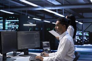 System administrator in data center checking equipment performance on computer after upgrading hardware. IT professional doing maintenance on storage devices in servers farm photo