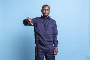 Security officer giving thumbs down dislike gesture in front of the camera, showing his disagreement about an idea. Guard shows his authority by denying something, negative symbol in studio. photo