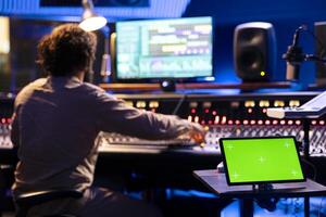 Tablet with isolated display in control room at professional recording studio, music producer editing and creating tracks for his new album. Sound designer works on mix and master with panel board. photo