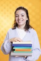 Portrait of joyous reading enthusiast woman holding stack of books, isolated over studio background. Cheerful nerd with pile of textbooks in arms used for academic learning photo