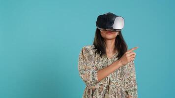 Indian woman wearing virtual reality headset, doing swiping gestures. Technology enthusiast using high tech futuristic modern VR gadget, isolated over studio background, camera A photo