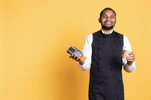 Professional friendly waiter showing the pos terminal with a credit card, symbolizing electronic payments for a meal. Restaurant employee works in a service oriented industry. photo