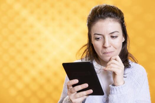 Woman reading captivating ebook on ereader device, enjoying hobby during leisure time. Bookaholic person with tablet in hands enjoying digital novel, scrolling on touchscreen, studio background photo